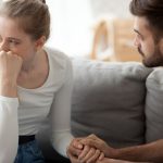 Man and woman sitting on couch crying and holding hands