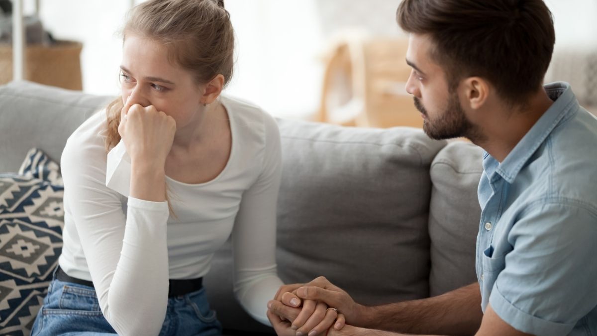 Man and woman sitting on couch crying and holding hands