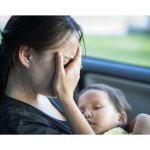 Mom crying in a car holding a sleeping infant